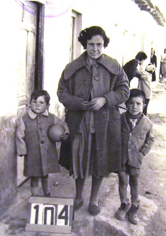 Las fotos son todo un documento de las condiciones de vida de los vecinos. Una madre con sus dos hijos en la puerta de su chabola en el Pozo del Huevo; el de la izquierda lleva un baln bajo el brazo. Al fondo, unas vecinas observan con curiosidad la escena asomadas a las puertas de sus casas. ( Foto: JJMANCHA / Vallecasweb.com)